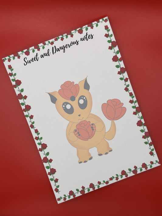 Notepad with a cute fictional creature design that is orange and has a rose on its head and a tail. The orange creature is holding a red rose and has big black eyes and black ears. The notepad has roses all around the four corners of the notepad and has a notepad heading of "Sweet and Dangerous Notes". The notepad is sitting on a red background.