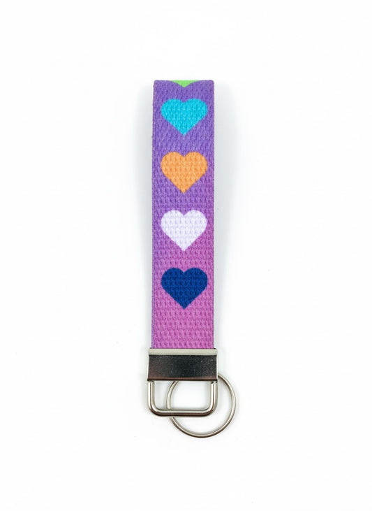 A purple fabric wristlet keychain featuring a vertical pattern of turquoise, orange, white, and dark blue hearts.