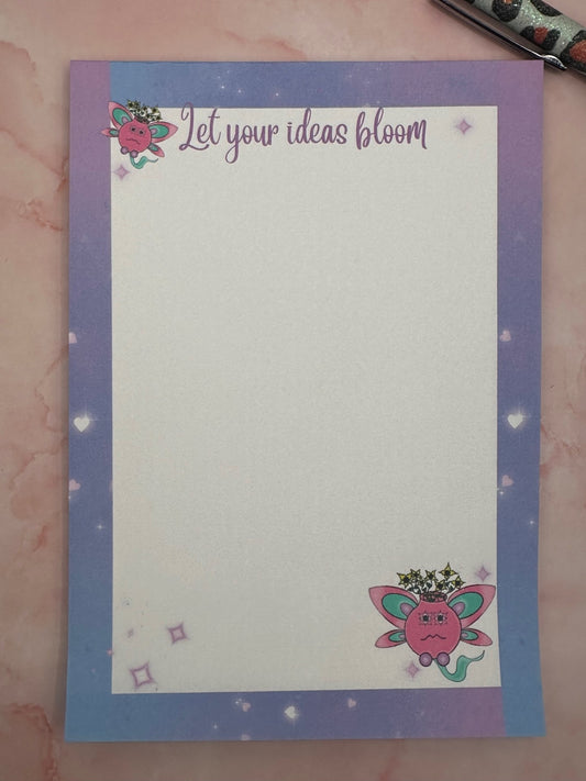 A notepad with fictional characters on top and bottom that are pink and turquoise color having yellow flowers come out of it. Around the notepad is purple color with hearts. The notepad heading states "let your ideas bloom". While the notepad is sitting on a pink background with a pen. 
