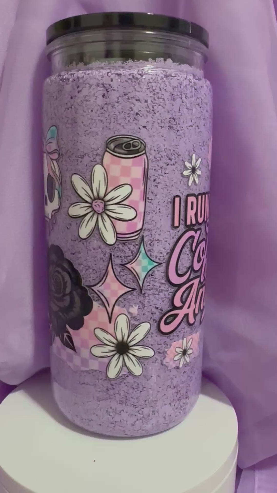 Purple snow globe tumbler with a black lid and straw, featuring the text: 'I RUN ON Coffee & Anxiety,' along with daisy and iced coffee illustrations.