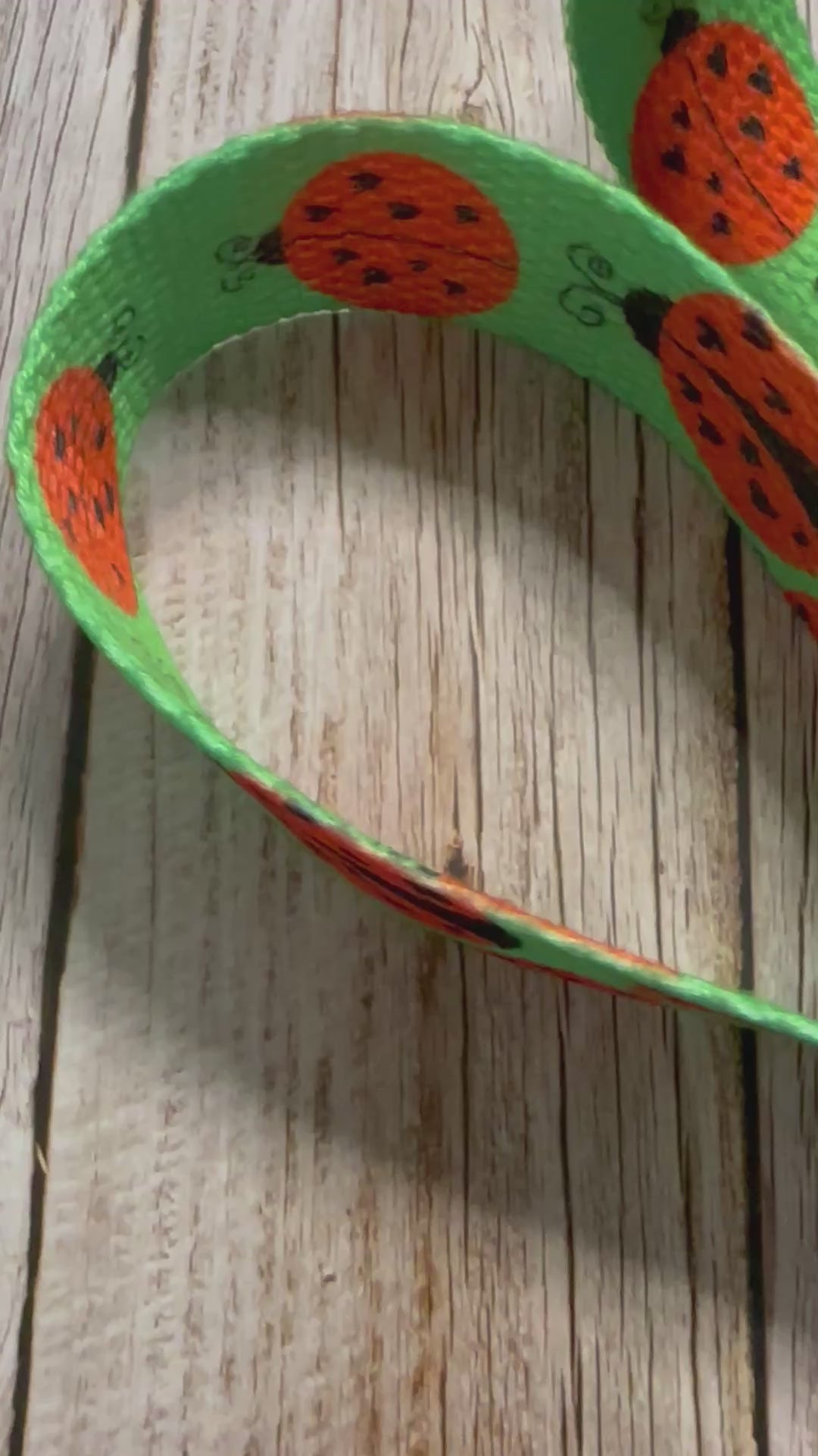 Video of the fabric wristlet keychain featuring a green background patterned with black and red ladybugs, shown on a light wooden surface.