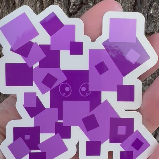 A sticker featuring a pixelated character made of various overlapping purple squares, with a small cartoon face visible in the center.