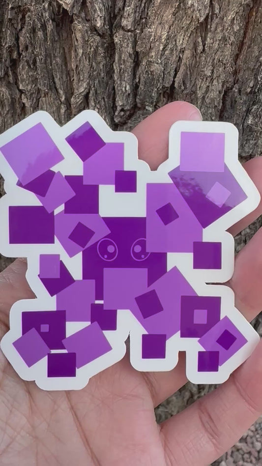 A sticker featuring a pixelated character made of various overlapping purple squares, with a small cartoon face visible in the center.