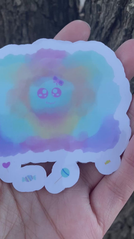 A sticker of a colorful, watercolor-style cloud shape in pastel blue, pink, yellow, and purple, featuring a cartoon face in the center and small candy illustrations along the bottom edge.