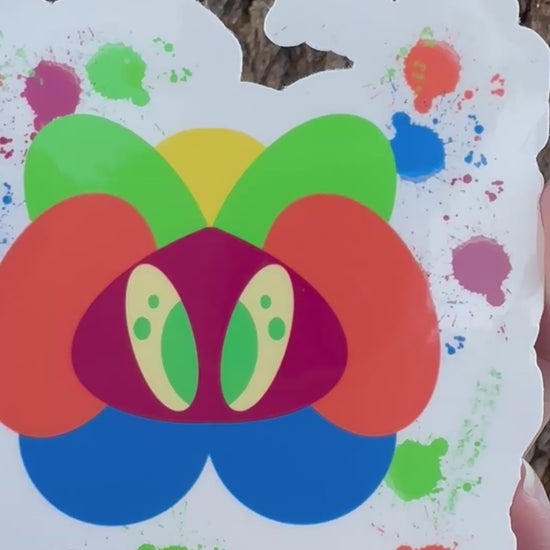 A sticker featuring an abstract, colorful creature made of layered organic shapes in orange, green, yellow, blue, red, and purple, surrounded by multi-colored paint splatters.