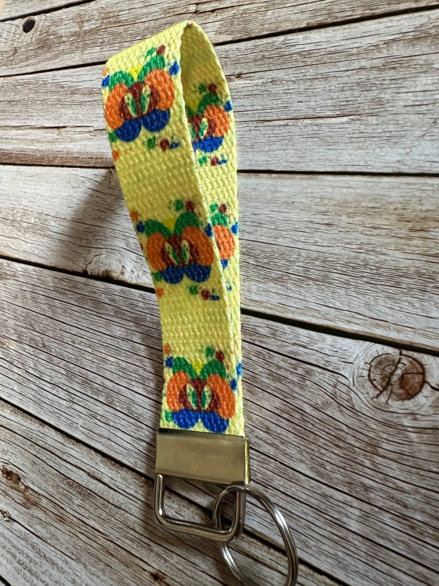 Yellow woven key fob wristlet with colorful design with fiction character splat on a wooden surface.