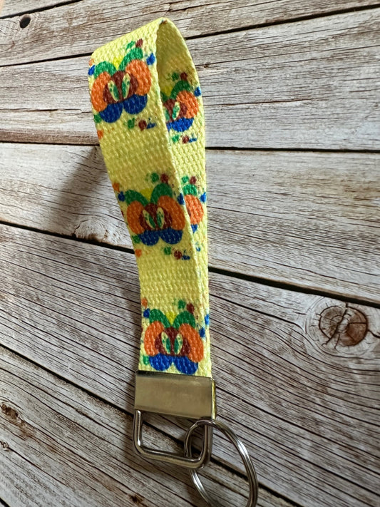 Yellow woven key fob wristlet with colorful design with fiction character splat on a wooden surface.