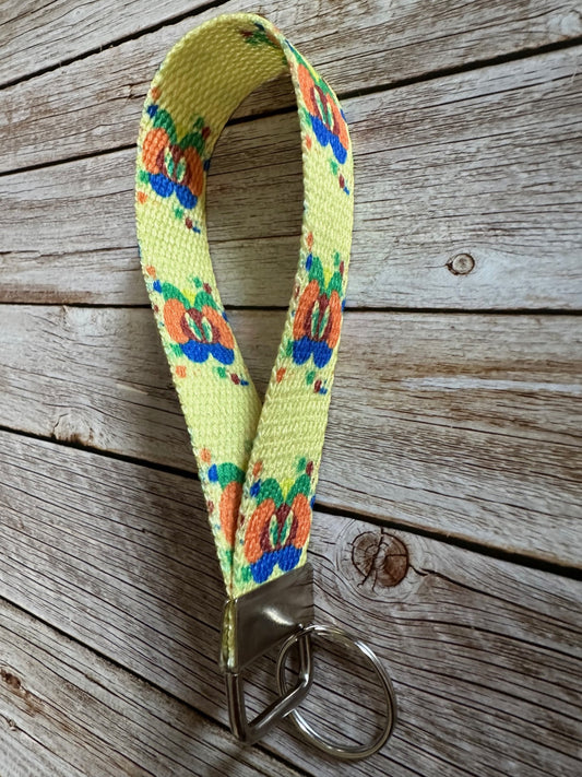 Yellow woven key fob wristlet with a colorful design featuring a fictional character splat on a wooden surface.