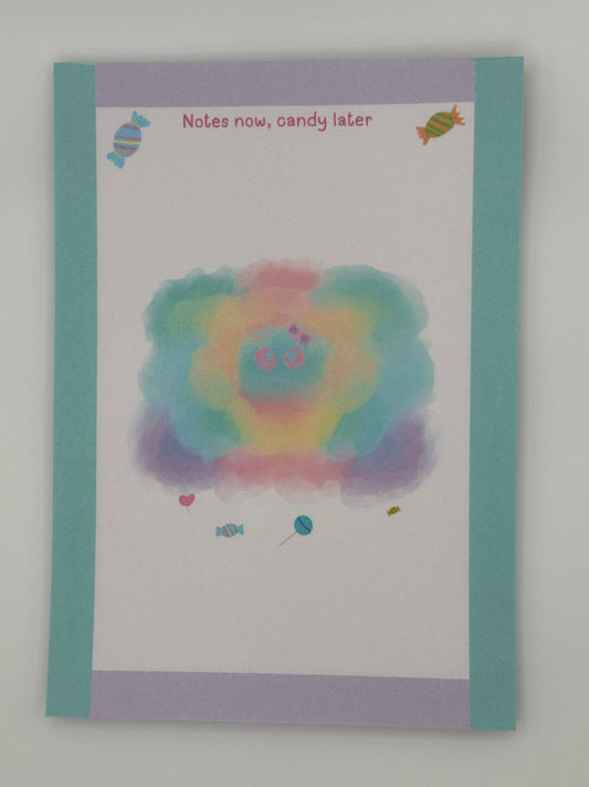 A notepad that has a pastel character that looks like a cloud. The character has a pink and purple bow with a pink eyes and smile. Candy is at the bottom of the cloudy pastel character and also on the top of the notepad. The notepad corner edges are light turquoise and light purple. The notepad heading "Notes now, candy later". The notepad is sitting on top of a white background.