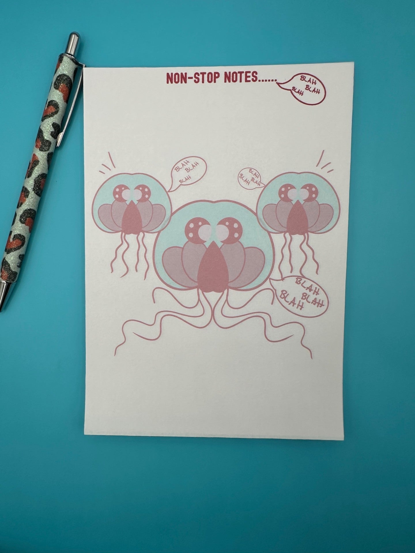 A notepad with three red jellyfish surrounded by the words "blah blah blah". The notepad heading has "non-stop notes.....". The notepad is sitting on a blue background with a pen.