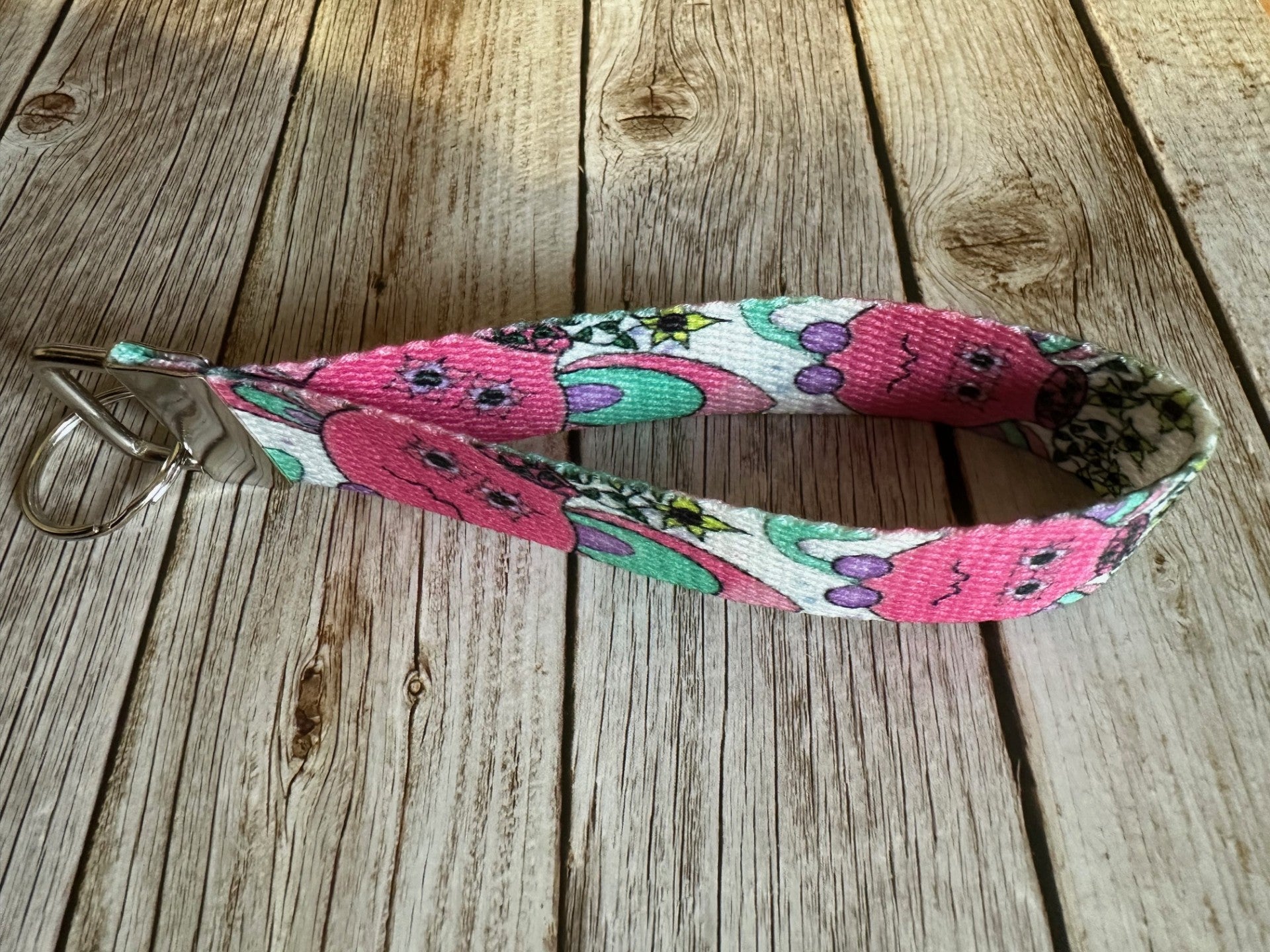 Wristlet with a pink flower pot illustrated design that has yellow flowers coming out of it, sitting on a wooden surface. 