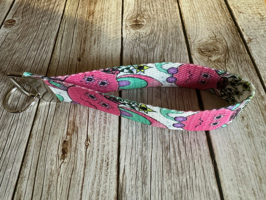 Wristlet with a pink flower pot illustrated design that has yellow flowers coming out of it, sitting on a wooden surface. 